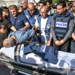 palestinian-journalists-in-blue-press-flak-vests-mourn-the-killing-of-a-colleague-by-israeli-forces